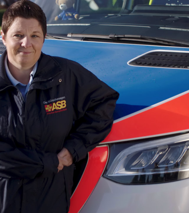 "37° Leben: Was am Ende zählt - Ehrenamtliche im Einsatz": Britta Dorstewitz (40) in einer Uniform des Arbeiter Samariterbundes lehnt sich mit ihrem Ellenbogen an einen Einsatzwagen des ASB.