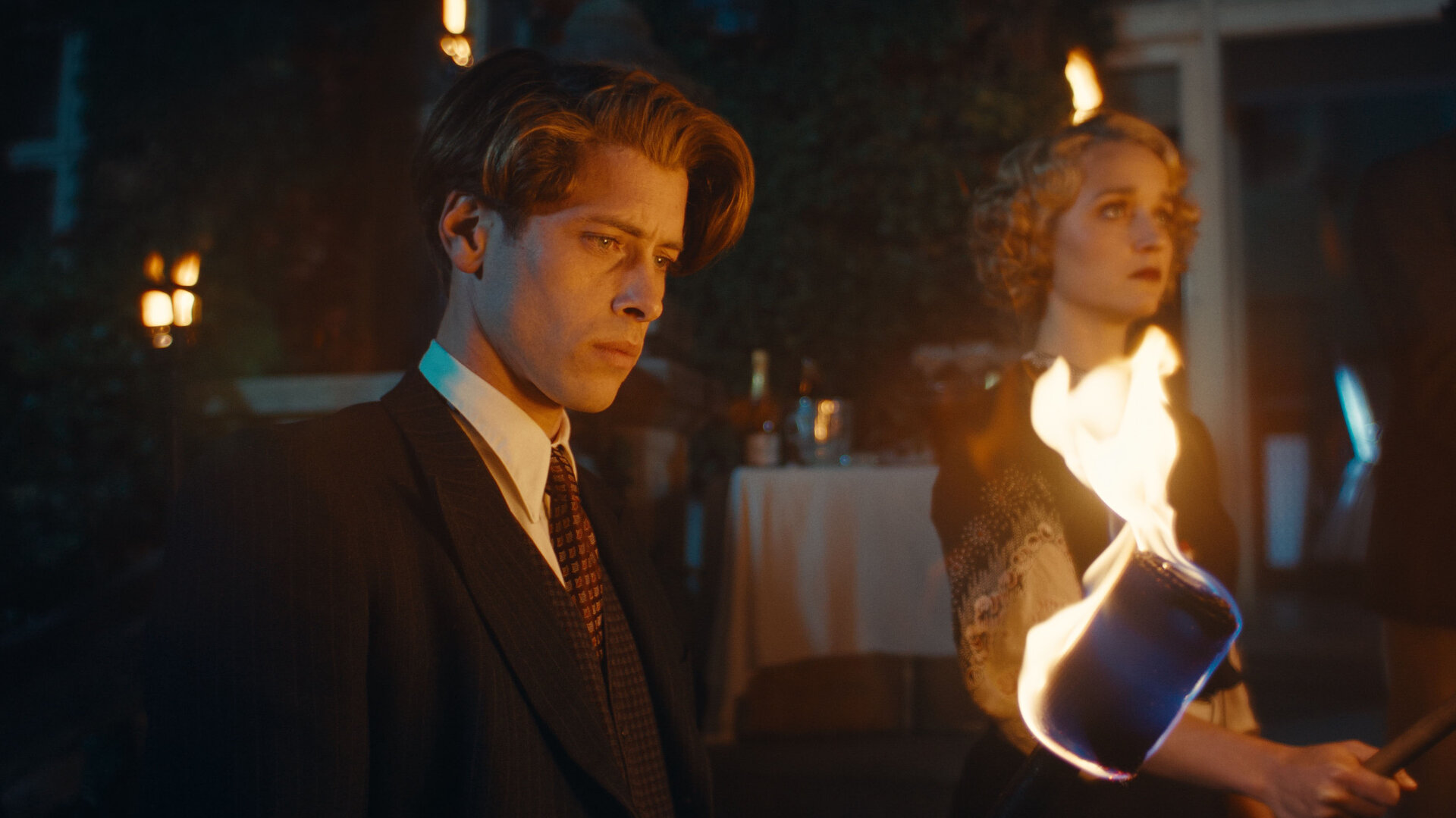 "This Is Not a Murder Mystery - Das Hummer-Telefon": René Magritte (Pierre Gervais) und Lee Miller (Florence Hall) stehen nebeneinander im Dunkeln. Im Vordergrund brennt eine Fackel, hinter den beiden sind weitere Lichter erkennbar.