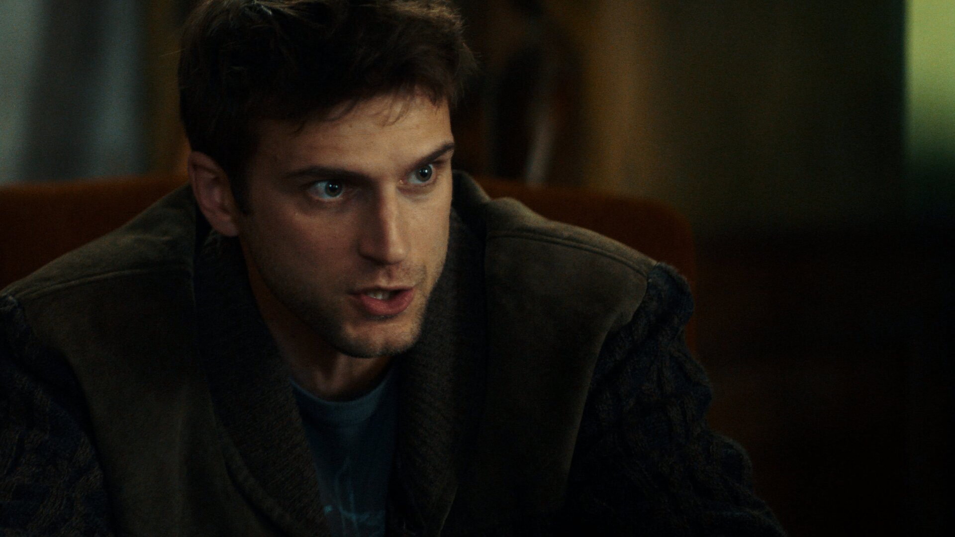 "Phoenix - Change Or Die: Die Entführer": Nahaufnahme: Polit-Aktivist Mathias Boissel (Léo Legrand) sitzt in dunkler Kleidung in einem Sessel mit brauner Lehne und spricht, sein intensiver Blick strahlt Überzeugungskraft aus.