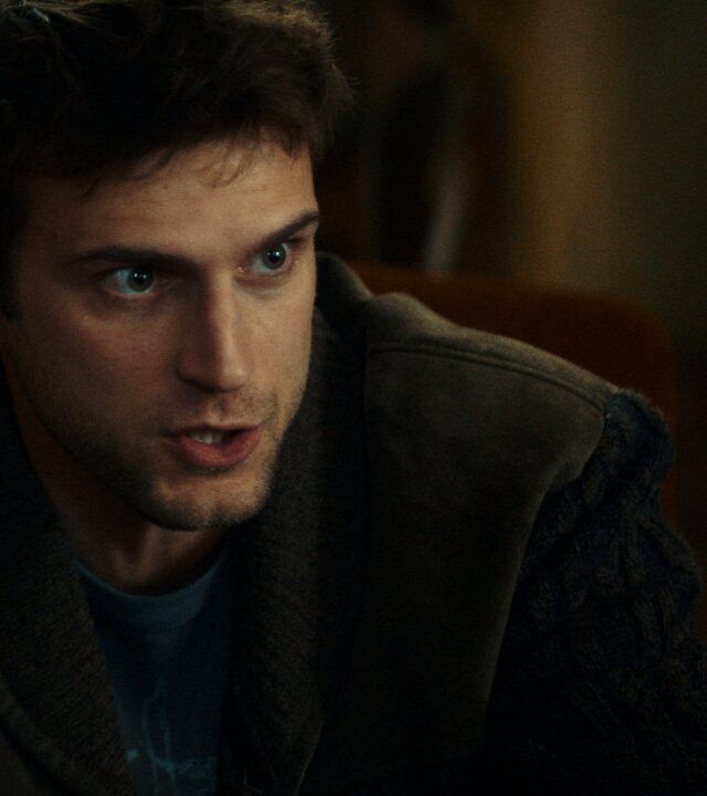 "Phoenix - Change Or Die: Die Entführer": Nahaufnahme: Polit-Aktivist Mathias Boissel (Léo Legrand) sitzt in dunkler Kleidung in einem Sessel mit brauner Lehne und spricht, sein intensiver Blick strahlt Überzeugungskraft aus.