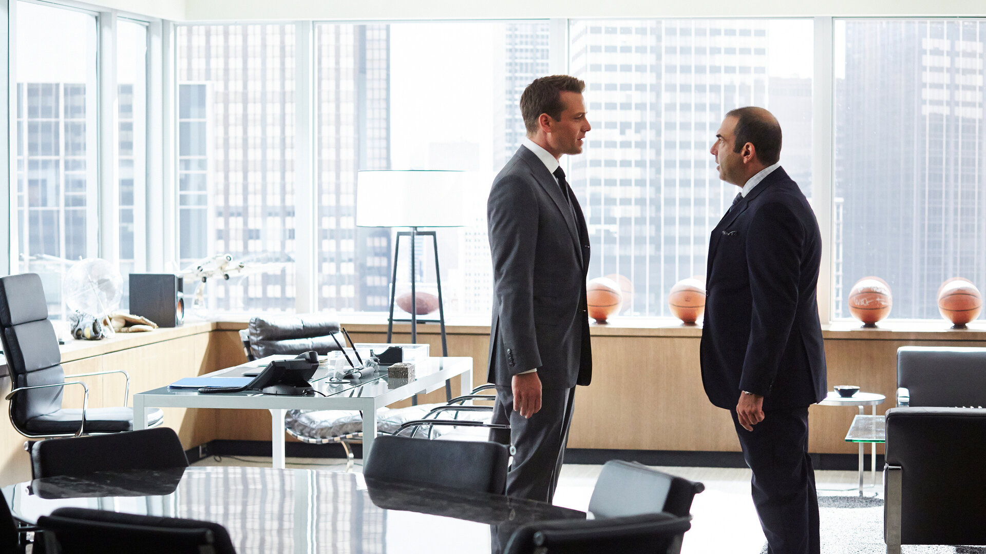 "Suits - Schweigen für Schweigen": Harvey (Gabriel Macht, l.) und Louis (Rick Hoffmann) stehen nah beieinander, sich zugewandt und führen ein intensives Gespräch. Im Hintergrund sind durch die große Glasfront Hochhausfassaden New Yorks zu erkennen.