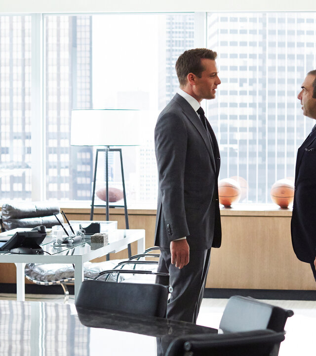 "Suits - Schweigen für Schweigen": Harvey (Gabriel Macht, l.) und Louis (Rick Hoffmann) stehen nah beieinander, sich zugewandt und führen ein intensives Gespräch. Im Hintergrund sind durch die große Glasfront Hochhausfassaden New Yorks zu erkennen.