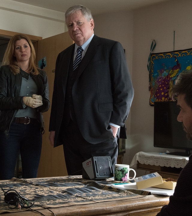 "Der Staatsanwalt - Die Enkelin": Christian Schubert (Simon Eckert), Kerstin Klar (Fiona Coors) und Bernd Reuther (Rainer Hunold) stehen in einem Zimmer vor Peter Blass (Thomas Scharff) und Paula Blass (Michelle Barthel). Die beiden sitzen hintereinander an einem Tisch und schauen die drei vor ihnen Stehenden an. Schubert zeigt ihnen das Foto einer Frau.