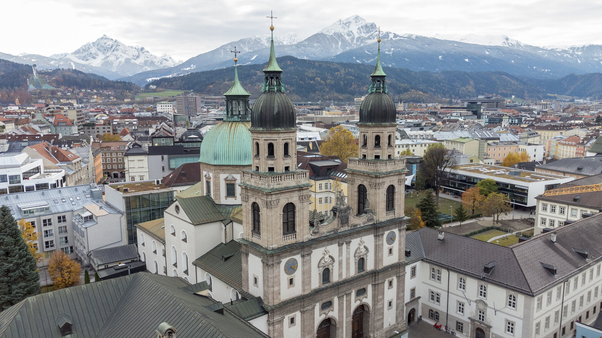 "Katholischer Gottesdienst - Menschheit erwache!": Luftaufnahme: Vor teils schneebedeckten Bergen liegt die Jesuitenkirche in Innsbruck mitten in einer urbanen Stadtlandschaft.