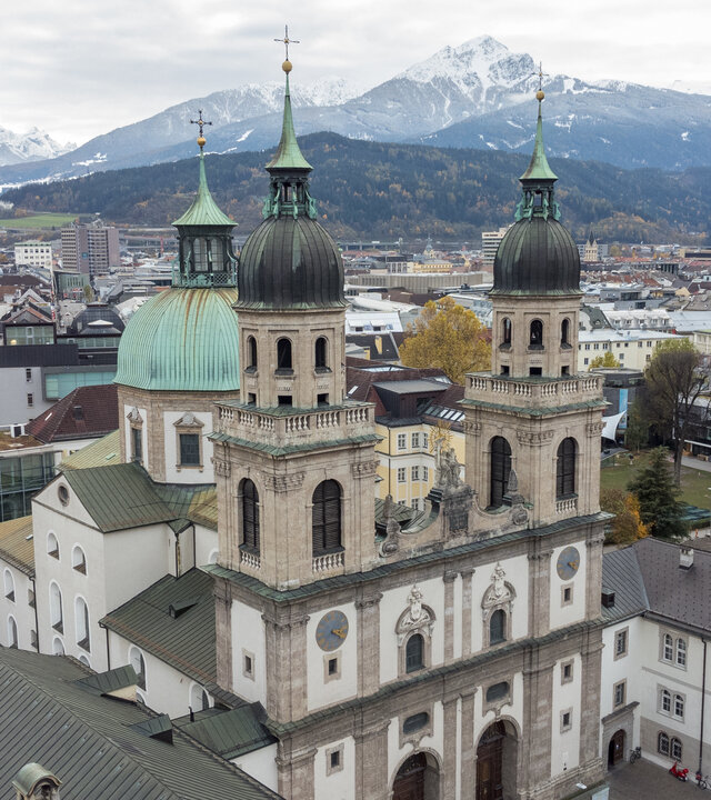 "Katholischer Gottesdienst - Menschheit erwache!": Luftaufnahme: Vor teils schneebedeckten Bergen liegt die Jesuitenkirche in Innsbruck mitten in einer urbanen Stadtlandschaft.