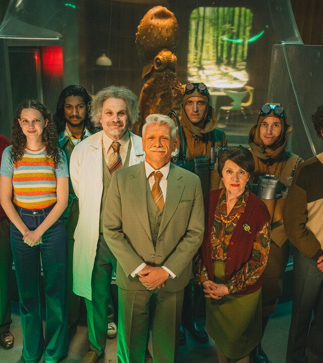 "We're on it, Comrades! - Unheimliche Begegnung der frostigen Art": Gruppenfoto: David Zajíc (Jiří Macháček), Eva (Darija Pavlovičová), Shushrut Kanchanmukh Balakrishnan (Kampan Soni), Dr. Karel Pavlas (Ján Jackuliak), Peter Čurko (Richard Stanke), Juna 2 (Tomáš Kobr), Professor Milada "Lada" Minterová (Lenka Termerová),  Juna 1 (Michal Kern) und Ingenieur Vojta Bek (Jan Cina) stehen versammelt in ihrem Institut und schauen leicht nach oben in die Kamera.