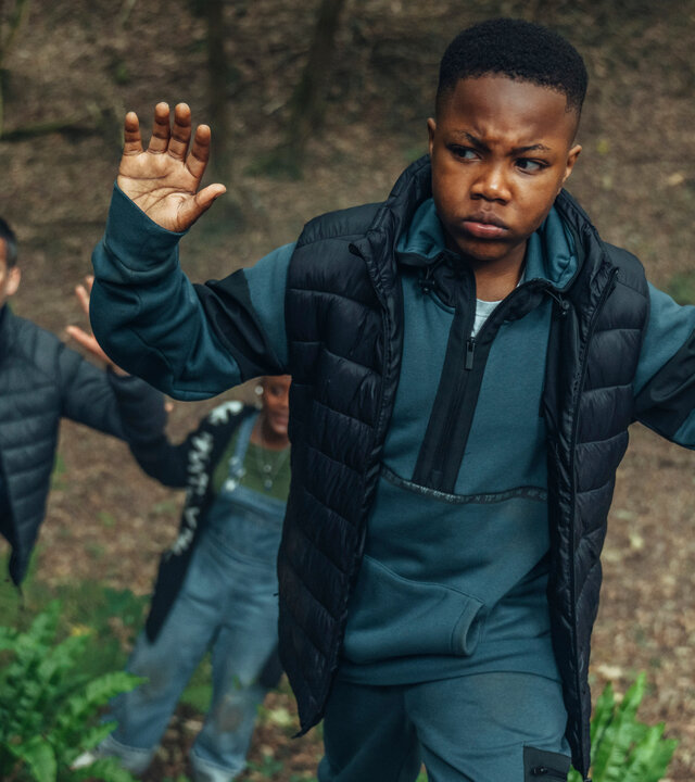 "Generation Z: Zur Hölle mit Dambury": Kofi (D’angelou Osei-Kissiedu), Michael (Robert James-Collier) und Karen (T'Nia Miller) gehen auf einer Böschung im Wald hintereinander her. Kofi und Michael heben die Hände. Karen ist nur zum Teil zu sehen.
