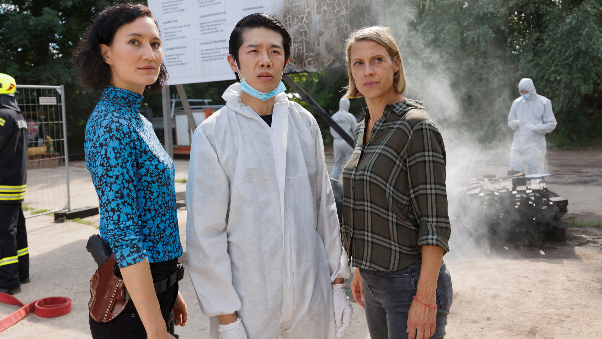 "SOKO Potsdam - Tatütata": Auf einem Firmengelände stehen Pauline Hobrecht (Agnes Decker), Spurensicherer Thomas Brandner (Yung Ngo) und Tamara Meurer (Anja Pahl). Im Hintergrund kümmern sich Spurensicherer und Feuerwehr um die durch den Brandanschlag verursachten Schäden.