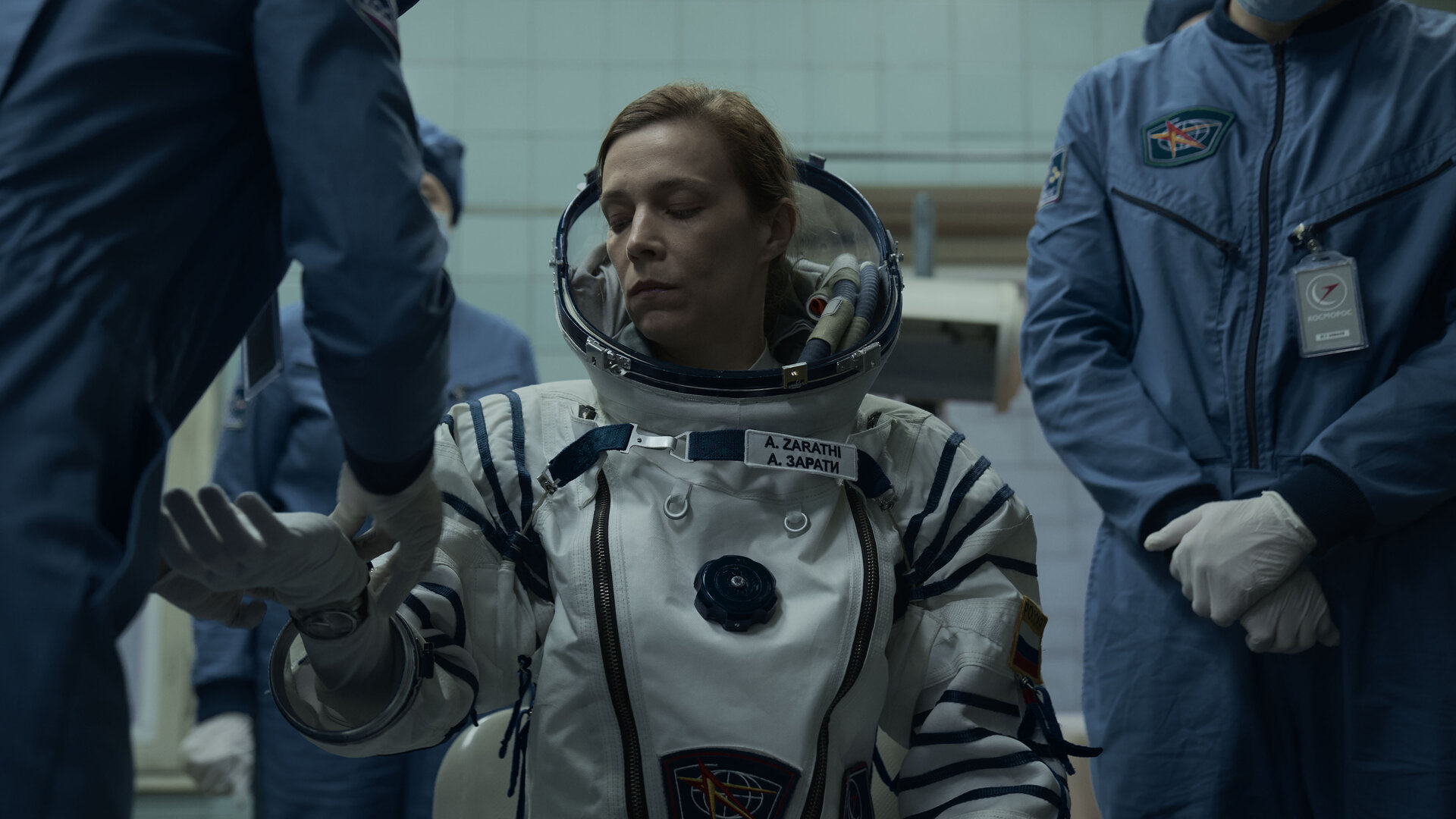 "Infiniti - Also sprach Zarathustra": Anna (Céline Sallette) sitzt angespannt inmitten mehrerer Personen mit Schutzanzügen, während ihr ein Raumanzug angelegt wird.