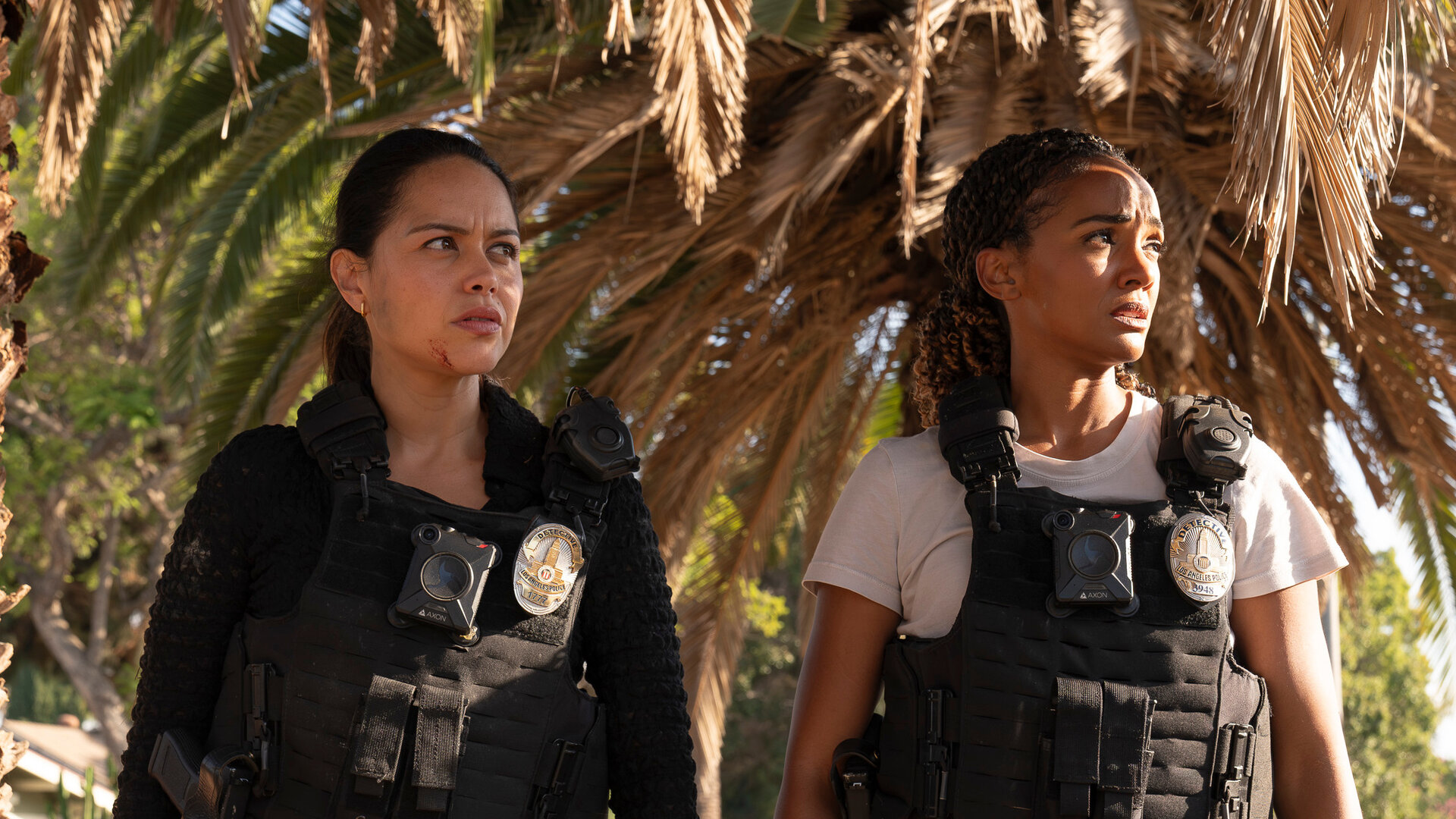 "The Rookie - Speed": Officer Lopez (Alyssa Diaz) und Detective Harper (Mekia Cox) stehen auf einem Gehweg unter einer ausladenden Palme. Sie tragen kugelsicher Westen. Beide blicken fragend zur Seite.