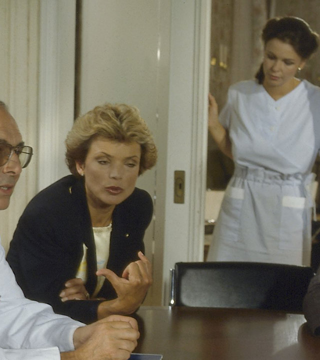 "Zwei Münchner in Hamburg - Extratouren": Julia (Uschi Glas) sitzt zusammen mit Dr. Sagerer (Elmar Wepper) und Dr. Schwarz (Karl-Friedrich Gerster) an einem Tisch. Sie diskutieren.