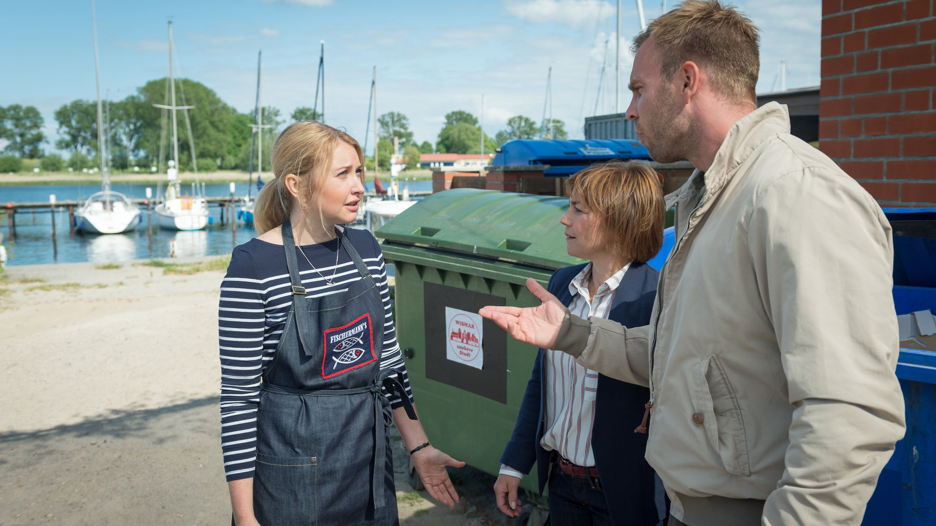 „SOKO Wismar – Die Kante von Wismar“: Katrin Börensen (Claudia Schmutzler) und Lars Pöhlmann (Dominic Boeer) sprechen mit Nadja Reisinger (Malina Ebert) hinter dem Hafencafé.
