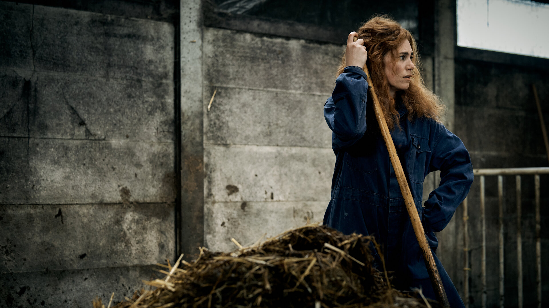 "Don't Fall, Dance - Auf der Überholspur": Emma (Hanna van Vliet) steht in einem Stall neben einem Misthaufen. Sie trägt einen Overall und hält ein Mistgabel in der Hand.