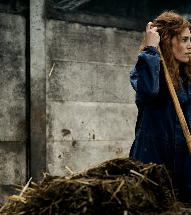 "Don't Fall, Dance - Auf der Überholspur": Emma (Hanna van Vliet) steht in einem Stall neben einem Misthaufen. Sie trägt einen Overall und hält ein Mistgabel in der Hand.