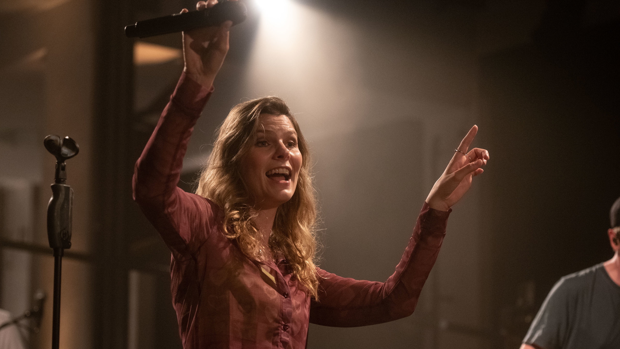 "Pop Around @ Bauhaus: Juli": Eine blonde Frau steht auf der Bühne  und lacht. Sie hat beide Hände in die Luft erhoben, in einer hält sie ein Mikro.