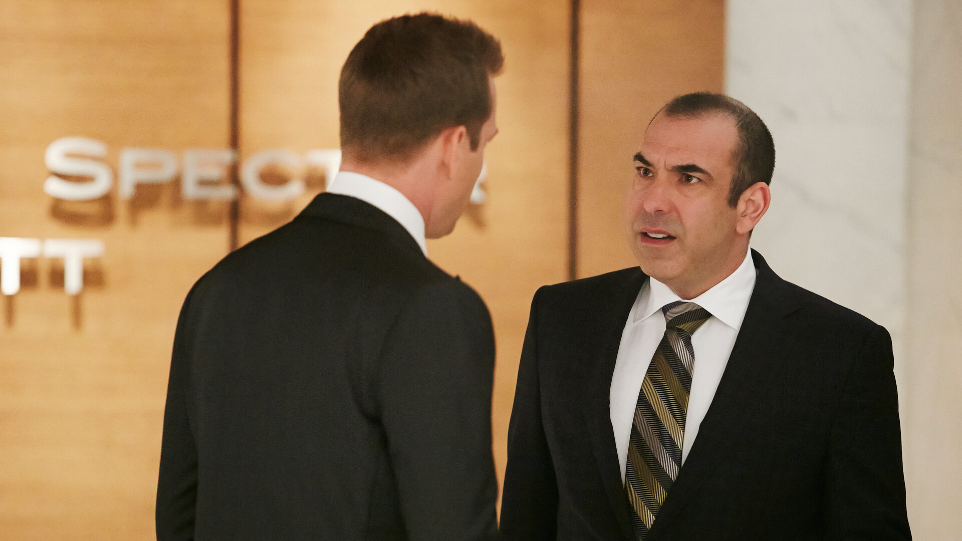 "Suits - Keine Frage des Geldes": Louis (Rick Hoffmann) und Harvey (Gabriel Macht) stehen sich im Flur der Kanzlei gegenüber. Louis schaut Harvey wütend an. Harvey steht mit dem Rücken zur Kamera.