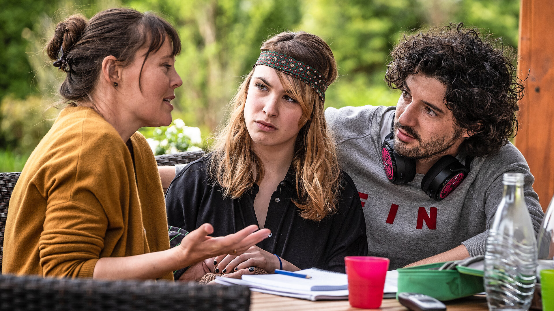 "Lena Lorenz - Außergewöhnlich einzigartig": An einem Gartentisch sitzen Saskia Mohrbutter (Zora Thiessen), Catharina Knuth (Victoria Schulz) und Sascha Reinhard (Manuel Mairhofer), der Kopfhörer um den Hals gelegt hat, und sprechen miteinander. Vor ihnen auf dem Tisch liegen Papiere.
