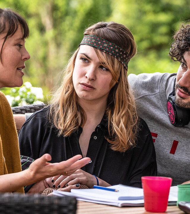 "Lena Lorenz - Außergewöhnlich einzigartig": An einem Gartentisch sitzen Saskia Mohrbutter (Zora Thiessen), Catharina Knuth (Victoria Schulz) und Sascha Reinhard (Manuel Mairhofer), der Kopfhörer um den Hals gelegt hat, und sprechen miteinander. Vor ihnen auf dem Tisch liegen Papiere.