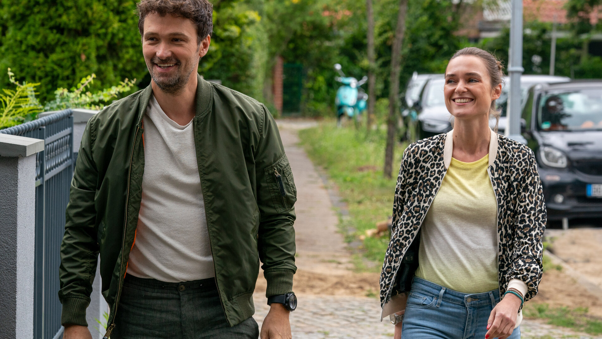 "Letzte Spur Berlin - Die Jäger": Alexander von Tal (Aleksandar Radenković) und Lucy Elbe (Josephin Busch) laufen leger nebeneinander auf einem Fußgängerweg. Beide lachen vergnügt.