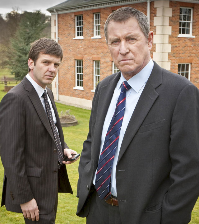 "Inspector Barnaby - Über den Dächern von Chattham": DS Ben Jones (Jason Hughes) und DCI Tom Barnaby (John Nettles) stehen nebeneinander auf einer Wiese, hinter ihnen ist ein großes Backsteinhaus zu sehen.