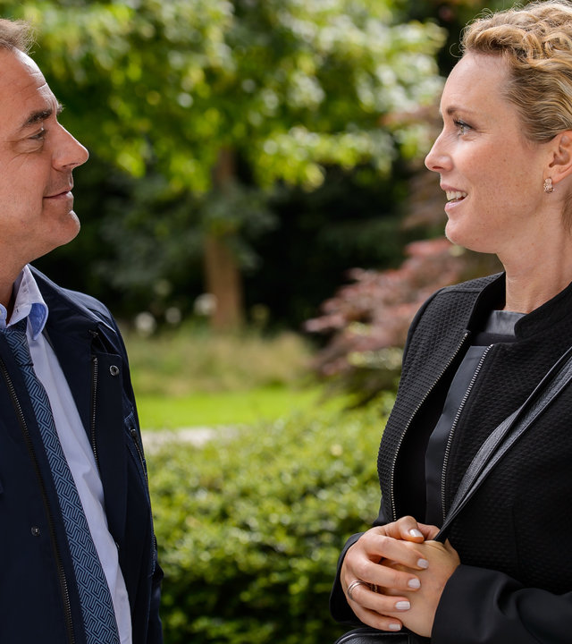 "Bettys Diagnose - Unter die Haut": Prof. Alexander von Arnstett (Florian Fitz) steht seiner Schwester Dr. Helena von Arnstett (Claudia Hiersche) im Freien gegenüber. Die beiden unterhalten sich lächelnd.