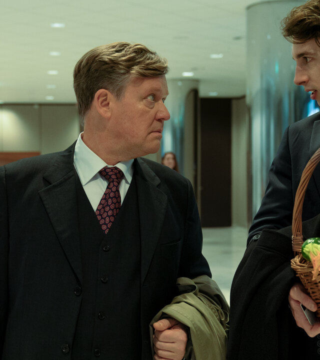 "Die Affäre Cum-Ex - Episode 1": In dem modernen Eingangsbereich eines Bürohauses spricht Bernd Hausner (Justus von Dohnányi) mit seinem Assistenten (Corvin Hummer), der einen Korb Zucchinis in der Hand hält.