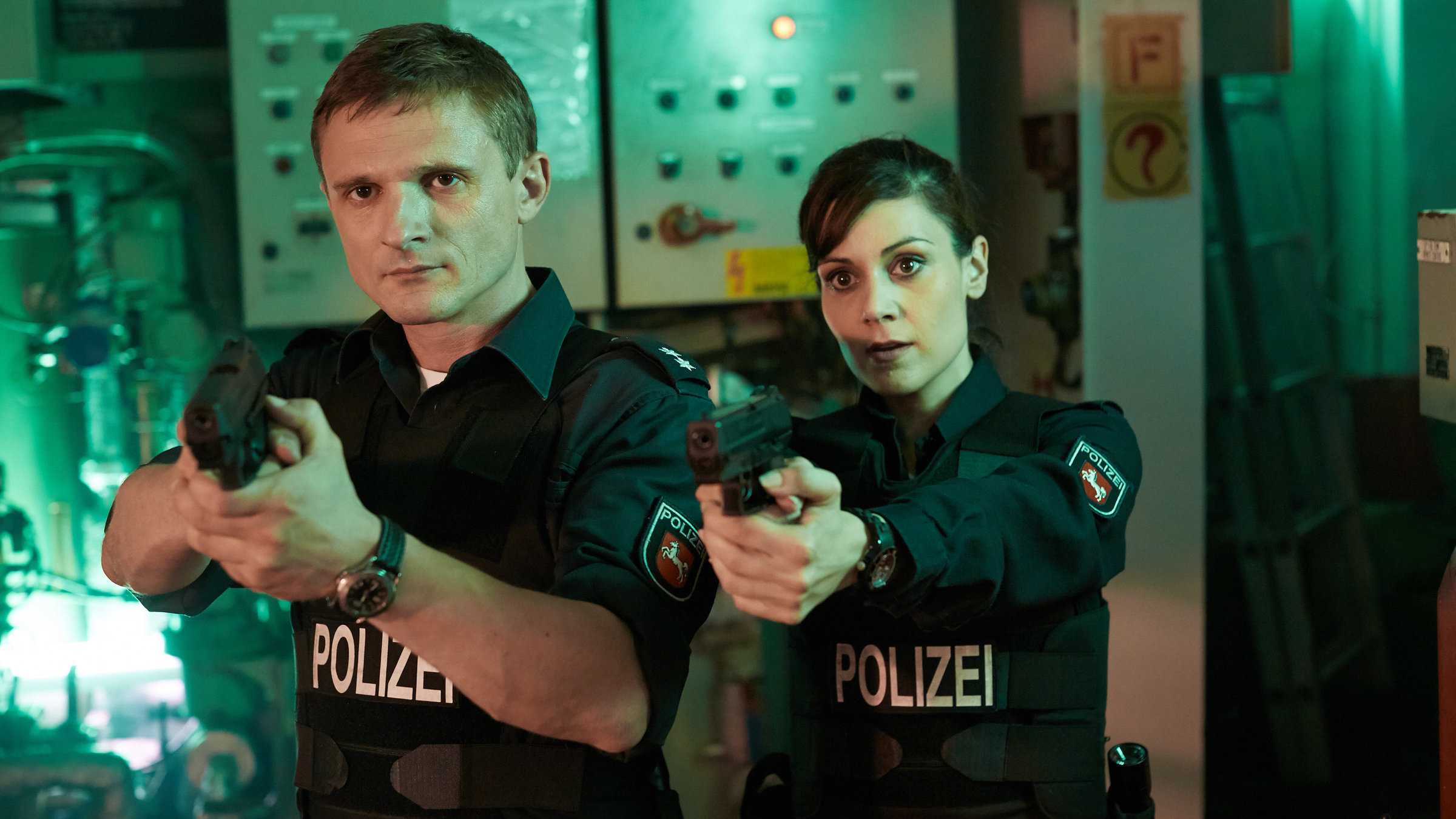"Friesland - Familiengeheimnisse": Jens Jensern (Florian Lukas) und Süher Özlügül (Sophie Dal) stehen nebeneinander und halten ihre Waffen im Anschlag.