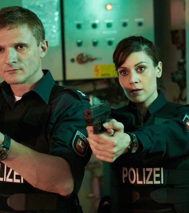 "Friesland - Familiengeheimnisse": Jens Jensern (Florian Lukas) und Süher Özlügül (Sophie Dal) stehen nebeneinander und halten ihre Waffen im Anschlag.