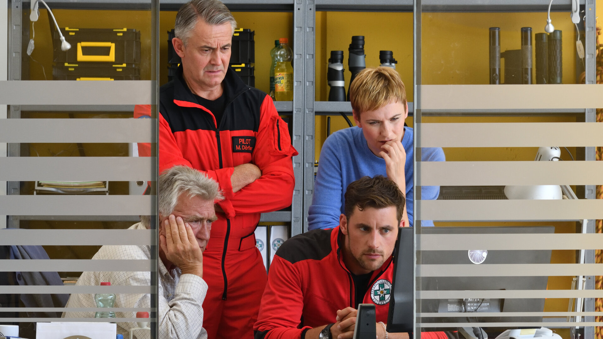 "Die Bergretter - Über den Wolken (1)": Franz (Heinz Maracek), Michael (Robert Lohr), Simon (Ferdinand Seebacher) und Verena (Gundula Niemeyer) befinden sich in einem Büro und schauen fassungslos in einen PC-Bildschirm.