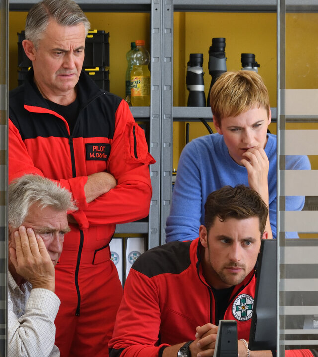 "Die Bergretter - Über den Wolken (1)": Franz (Heinz Maracek), Michael (Robert Lohr), Simon (Ferdinand Seebacher) und Verena (Gundula Niemeyer) befinden sich in einem Büro und schauen fassungslos in einen PC-Bildschirm.