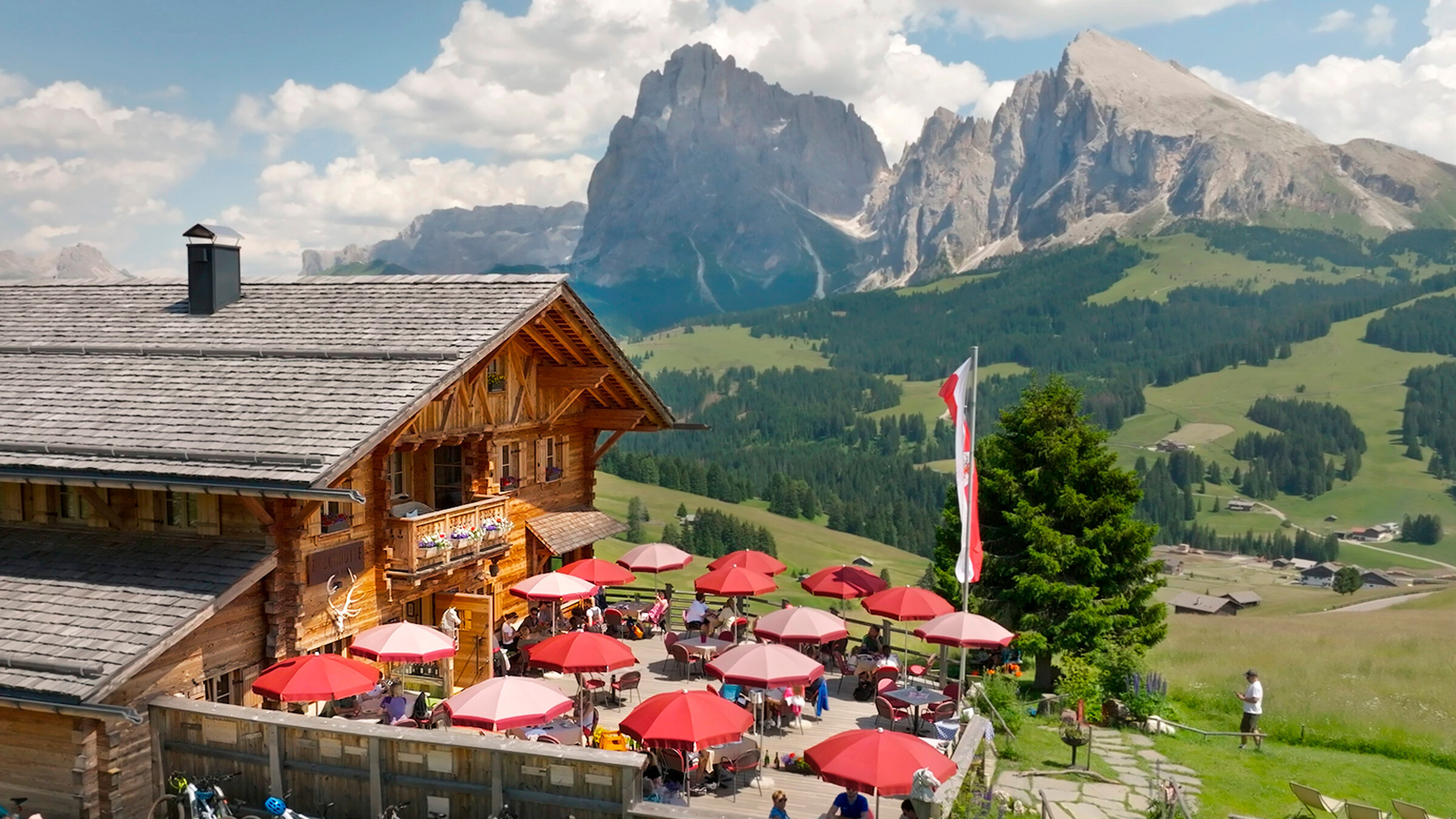 "Die Dolomiten - Sommer in den italienischen Alpen": Beliebter Rastplatz in den Dolomiten im Norden Italiens: Auf der Seiseralm ist die Terrasse der Rauchhütte gut besucht. Im Hintergrund Langkofel und Plattkofel.