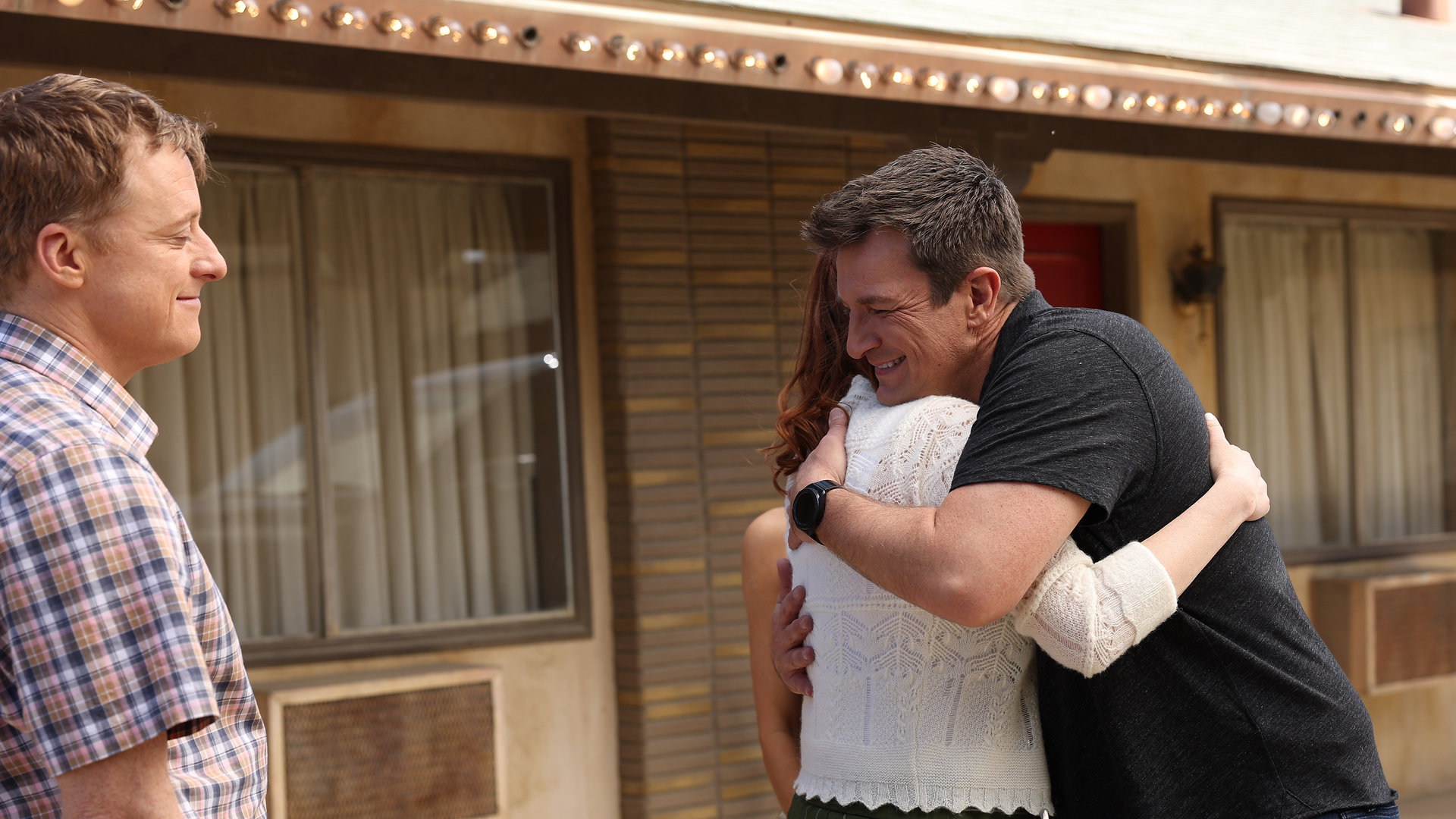 "The Rookie - In der Einöde": Nolan (Nathan Fillion) umarmt Ellroys Freundin vor einem ruhigen Motel, während Ellroy (Alan Tudyk) dabei zusieht.