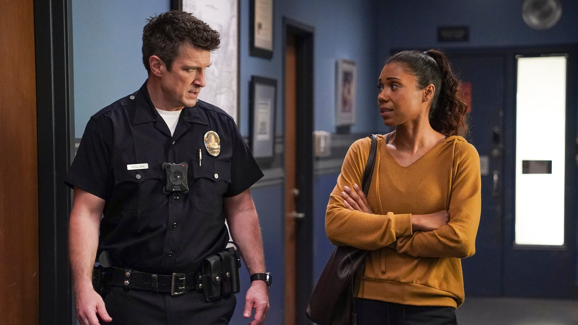 "The Rookie - Überleben": Nolan (Nathan Fillion) und Professorin Ryan (Toks Olagundoye) laufen einen Gang entlang. Während Nolan Ryan ernst anschaut, sieht Ryan verunsichert zu ihm rüber.