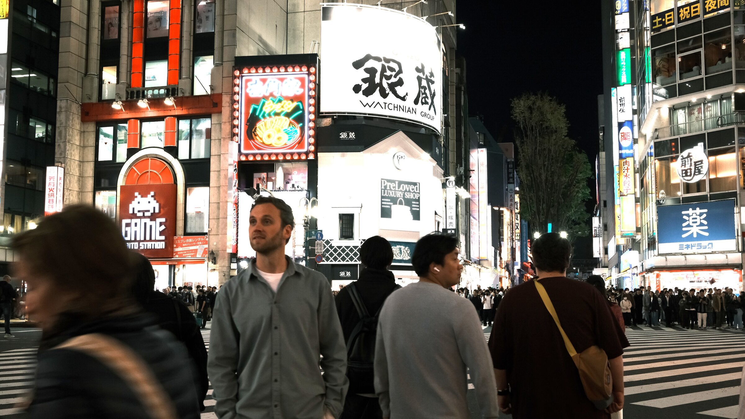"Terra X: WeltstÃ¤dte - Tokyo": Leon Windscheid steht nachts auf einer StraÃenkreuzung in Tokyo. Hinter ihm leuchten die Schilder an den HochhÃ¤usern in bunten Farben.