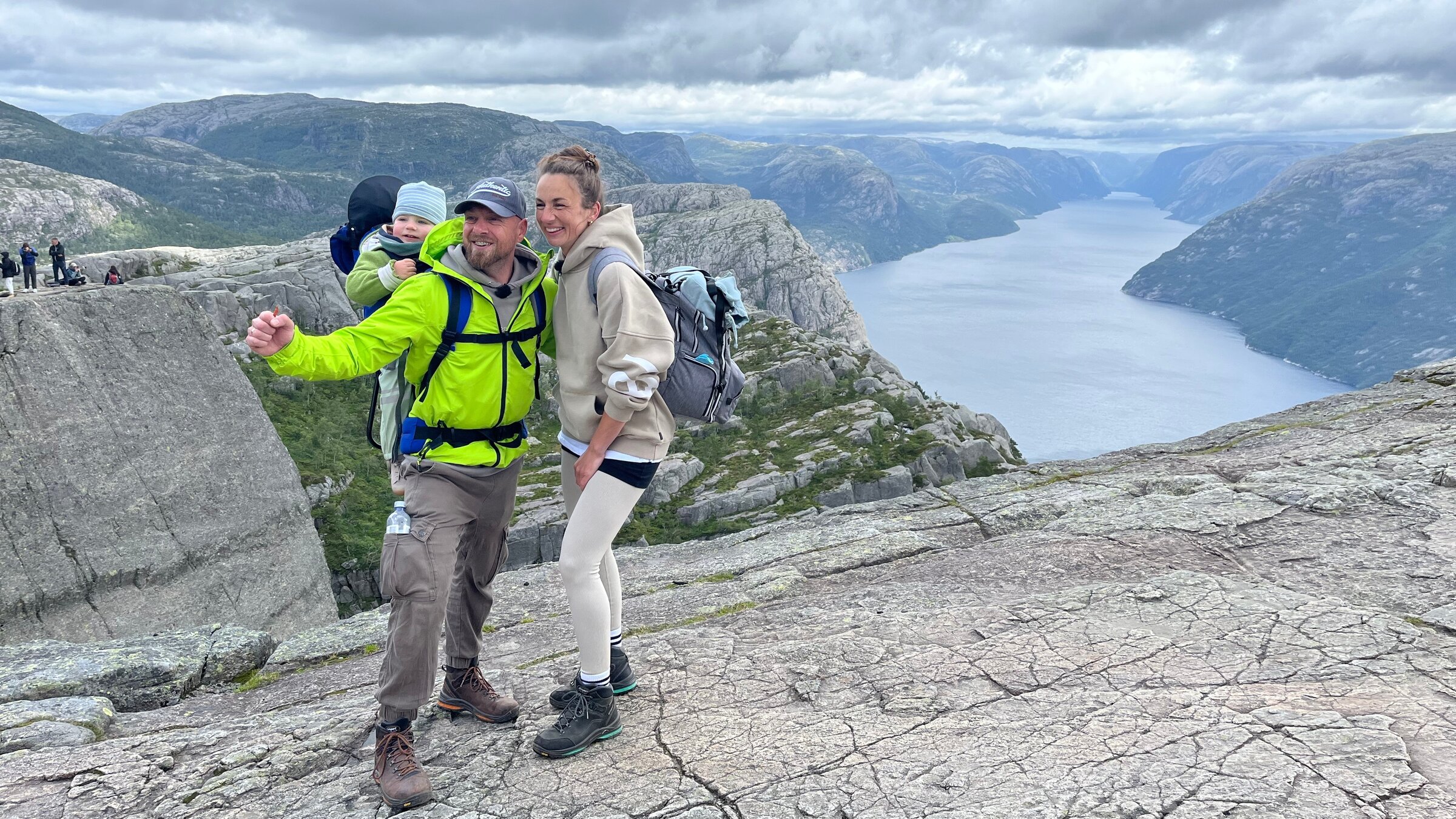 "ZDF.reportage: Norwegen am Limit - Urlauberflut im Norden": Robert und Yvonne stehen auf einem Felsvorsprung, Sohn Paul ist auf dem Rücken von Robert. Im Hintergrund ist eine Flusslandschaft zu sehen.