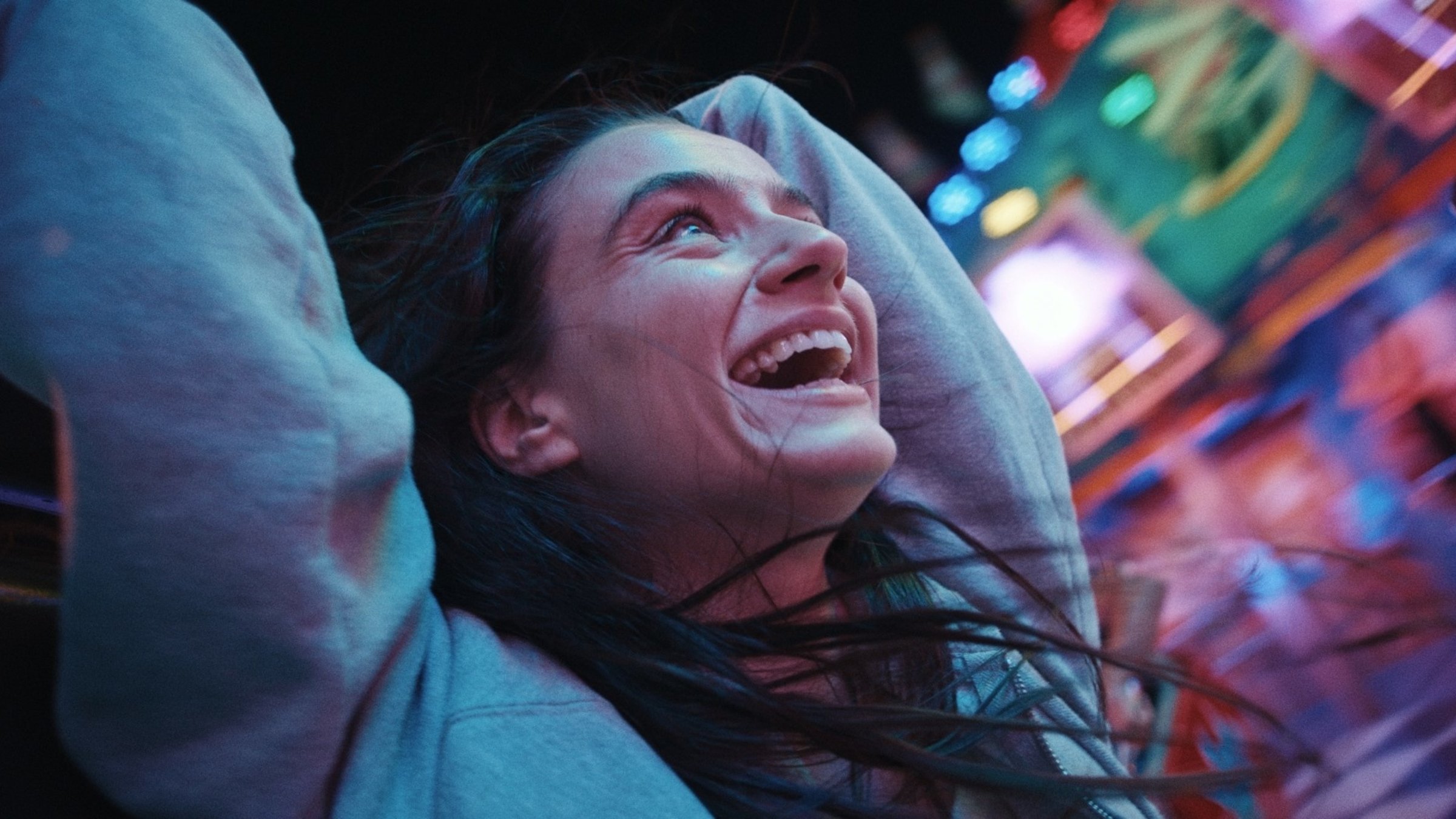 "Zwischen uns die Nacht": Marie (Laura Balzer) lacht glücklich und hat die Arme nach oben gehoben. Ihre Haare fliegen wild umher. Im Hintergrund sind die bunten Lichter des Jahrmarkts zu sehen.