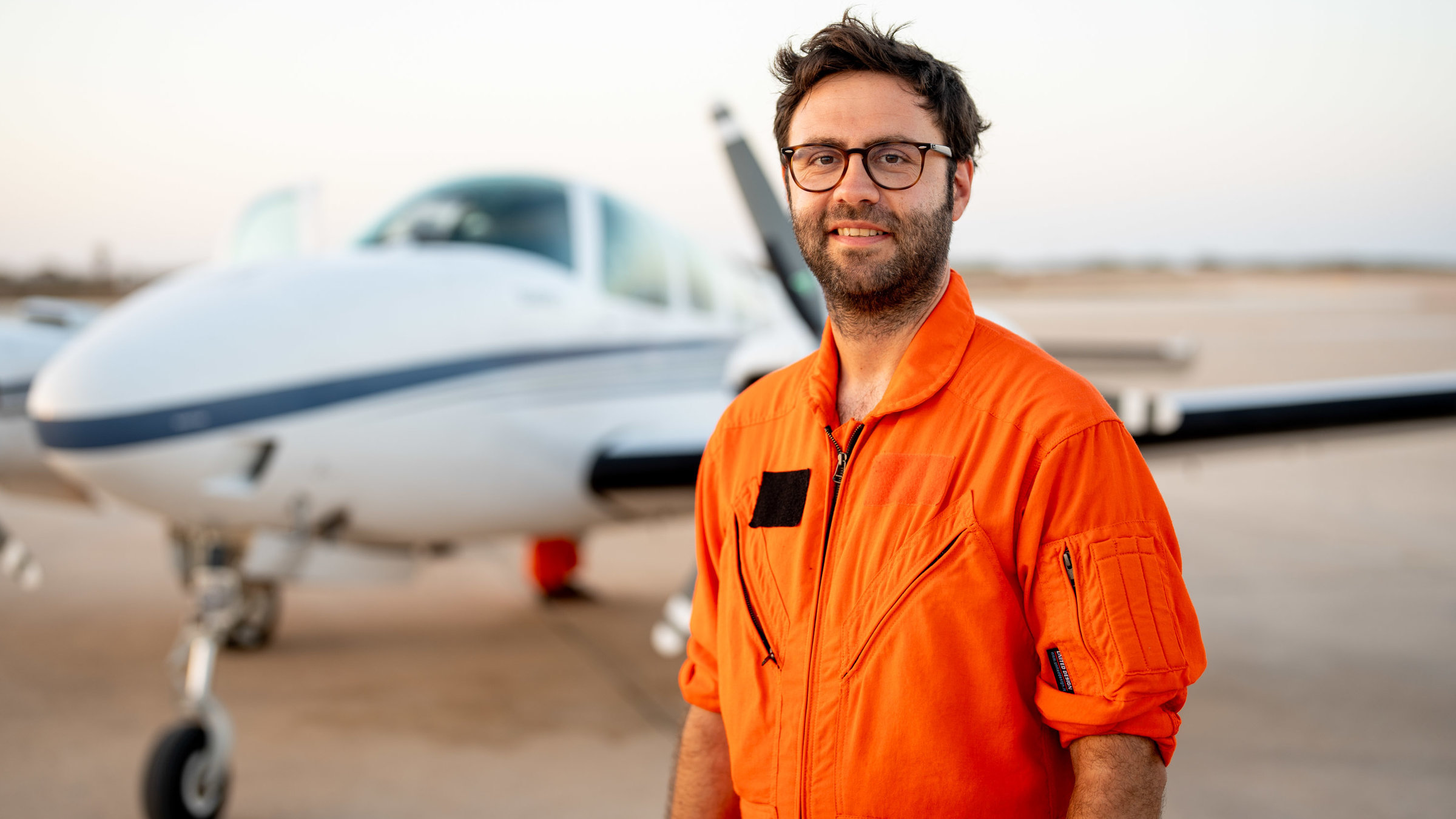 "37° Leben - Seenotrettung aus der Luft": Manos Radisoglou steht vor dem Einsatzflugzeug "Seabird" und lacht in die Kamera.
