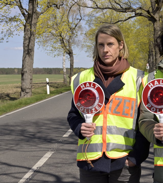 "SOKO Potsdam - Mensch und Maschine": Mitten auf einer Landstraße stehen Tamara Meurer (Anja Pahl) und Pauline Hobrecht (Agnes Decker). Beide tragen eine Polizei-Warnweste und halten eine Verkehrskelle in Richtung Kamera.