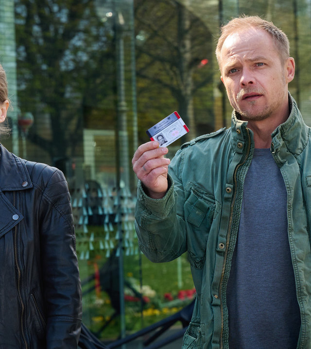 "Die Toten vom Bodensee - Das zweite Gesicht": Hannah Zeiler (Nora Waldstätten) und Micha Oberländer (Matthias Koeberlin) laufen nebeneinander eine Straße entlang. Micha Oberländer hält einen Ausweis in der Hand.