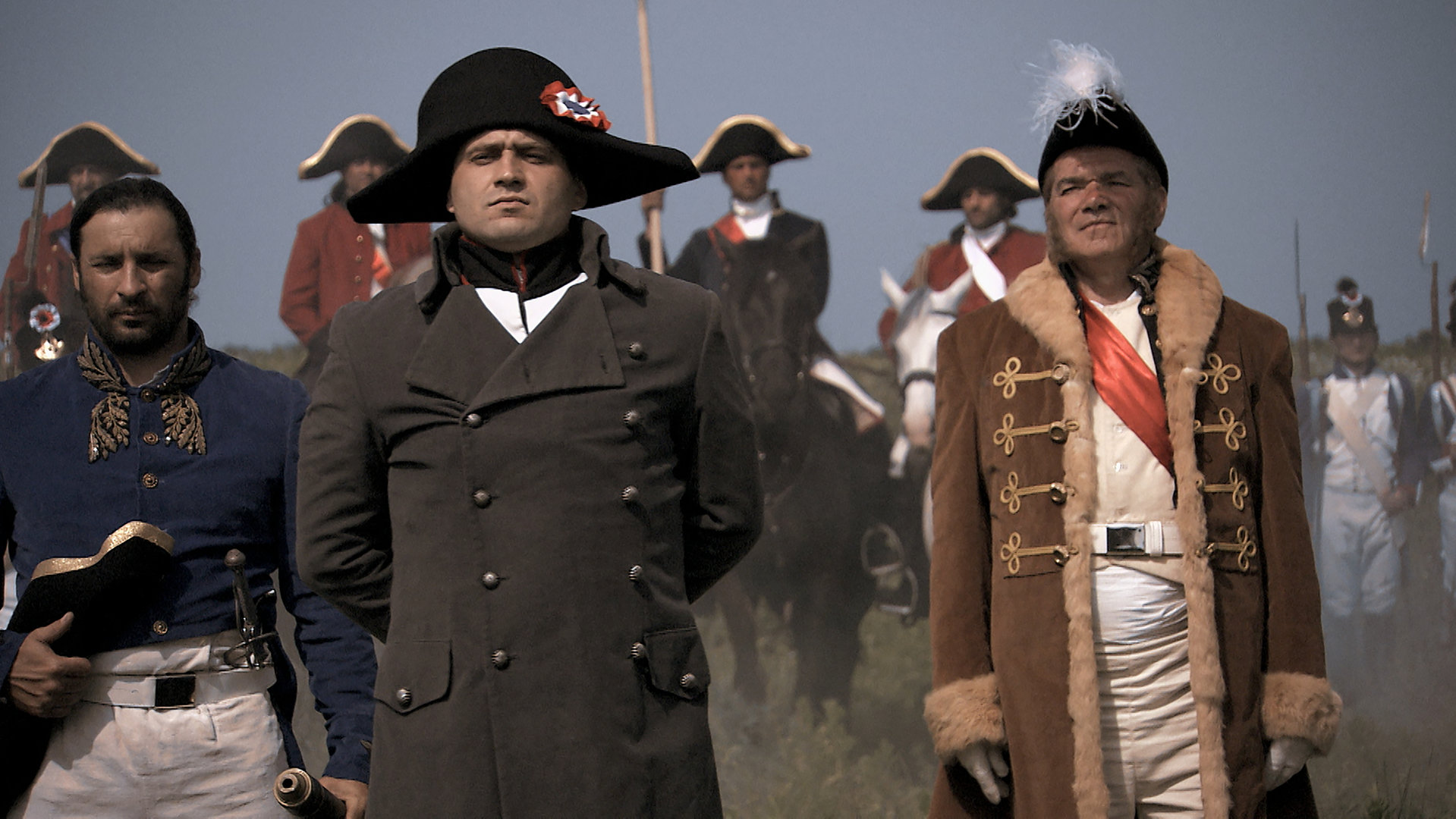 "Die glorreichen 10 - Die krassesten Raubzüge der Geschichte": Spielszene. Napoleon steht, umgeben von Offizieren, am Rande eines Schlachtfelds und schaut mit hinter dem Rücken verschränkten Armen, geschwelter Brust und erhobenen Kinn Richtung Kamera.