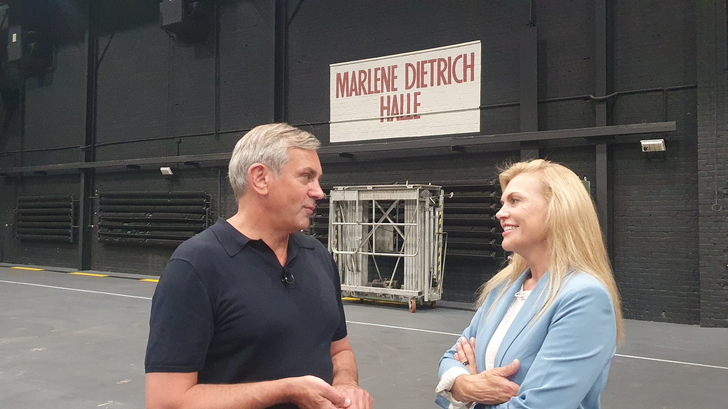 "Kaminer Inside: Filmstadt Babelsberg": Kaminer und Anna Loos stehen vor einer geschwärzten Backsteinwand und reden miteinander, an der Wand steht groß in roten Lettern auf Weiß: Marlene Dietrich Halle