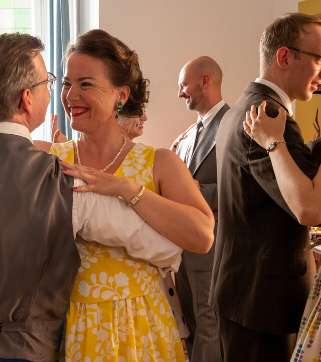 "SOKO Stuttgart - Die goldenen 50er": In einem im Stil der 50er-Jahre eingerichteten Wohnzimmer tanzt das Ehepaar Ina (Josephine Ehlert) und Georg Trapp (Dominik Klingberg) einen Standardtanz. Sie strahlen sich glücklich an. Um sie herum tanzen weitere Paare (Komparsen). Alle tragen Kleidung im Stil der 50er-Jahre.