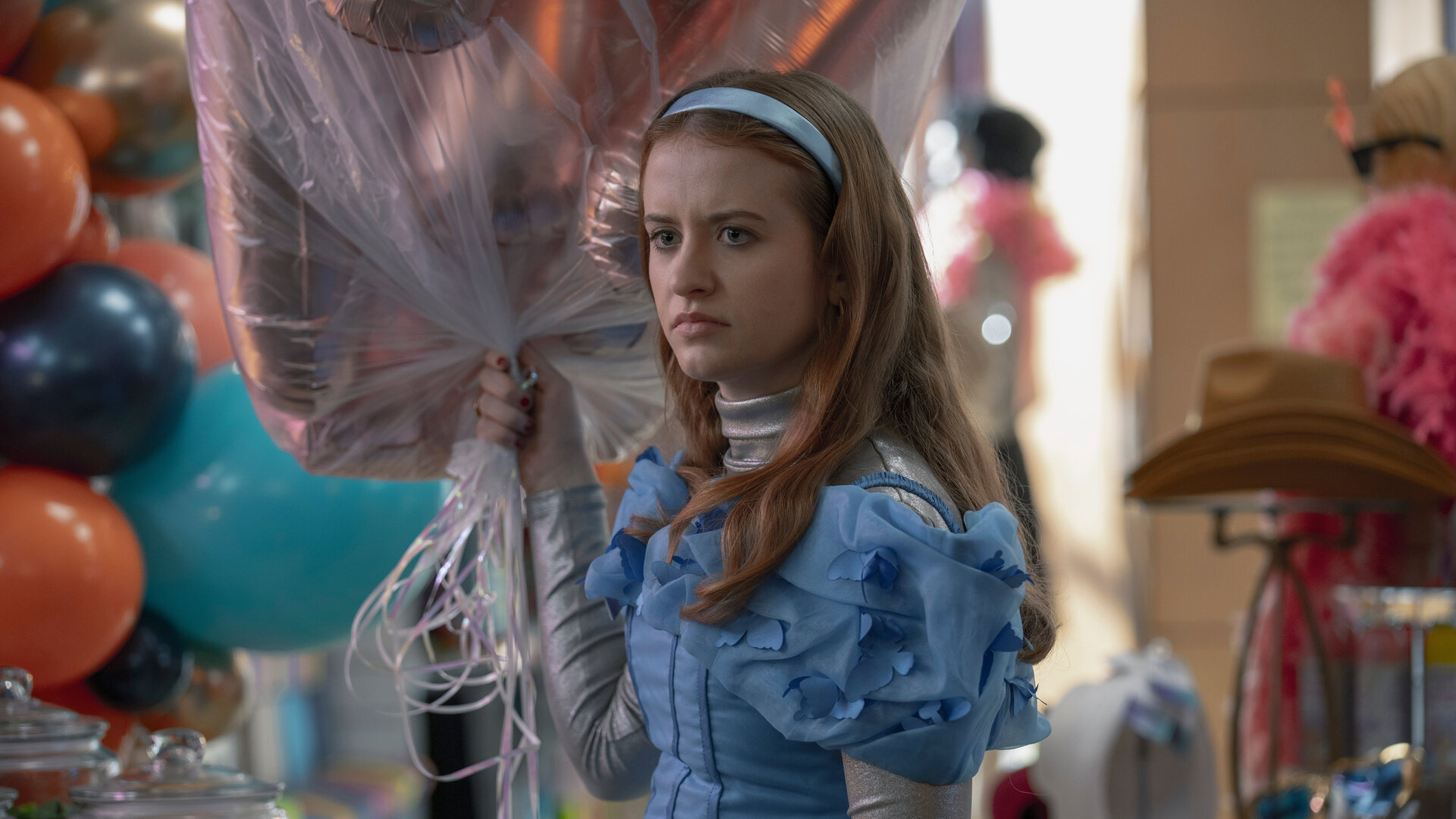 "Extraordinary - Habenichtse": Jen (Máiréad Tyers) steht grimmig blickend in einem Geschäft. In ihrer Hand hält sie ein Strauß Helium-Luftballons.