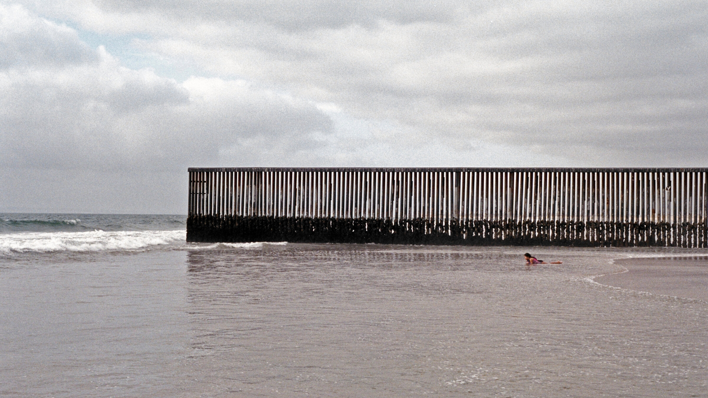 "Wenn der Nebel kommt": Totale von einem Strand, an dem ein hoher Zaun aus Metallstäben vom Land ins Meer führt.