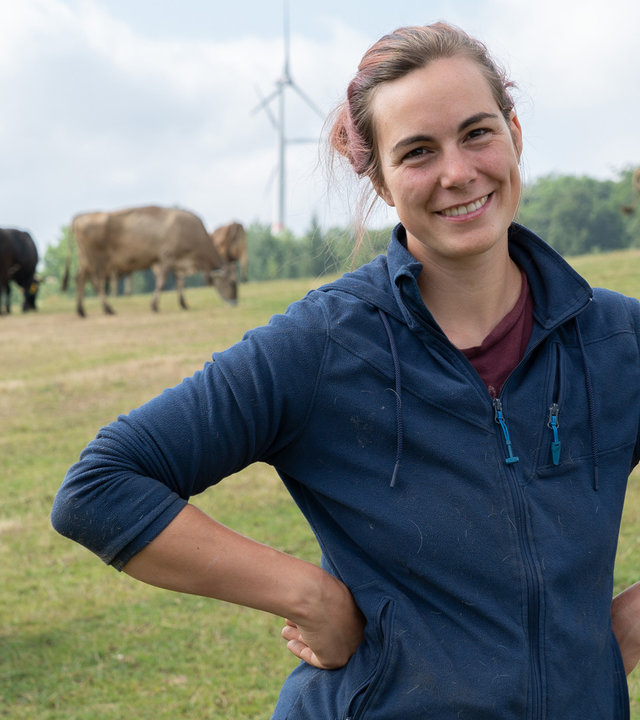 "37°Leben: Anders ackern - Nächste Generation": Marie Tigges steht auf einer Wiese mit Kühen im Hintergrund und lächelt in die Kamera.