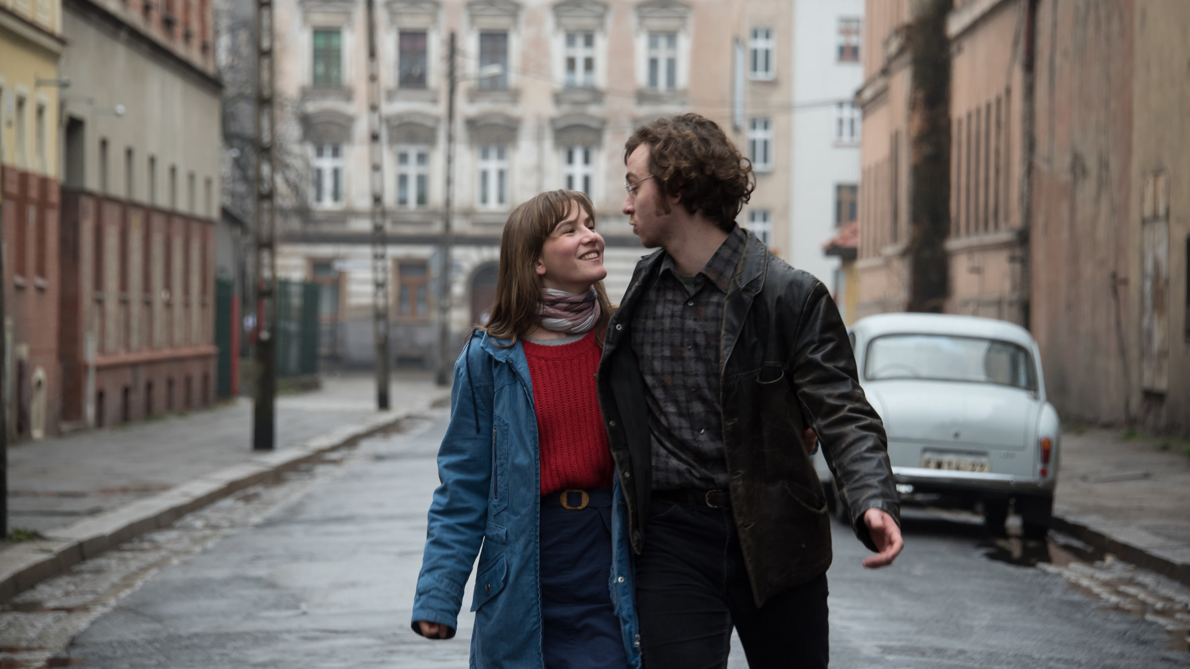 "Zwischen uns die Mauer": Anna (Lea Freund) und Philipp (Tim Bülow) laufen Arm in Arm durch eine Straße mit typischen Mietshäusern aus Ostberlin. Sie sehen sich verliebt in die Augen.