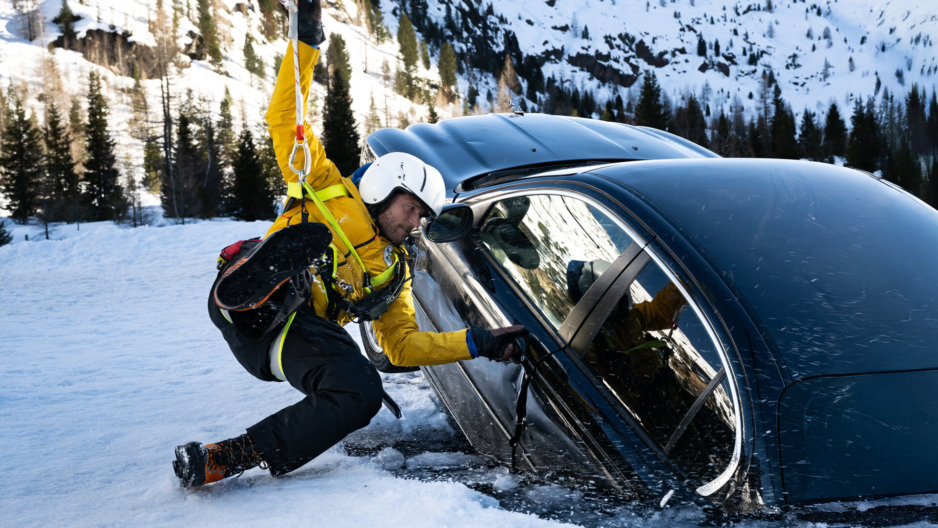 "Die Bergretter: Die letzte Rettung": In einer verschneiten Berglandschaft: Bergretter Markus Kofler (Sebastian StrÃ¶bel) hÃ¤ngt am Rettungsseil des Helikopters. Er versucht die TÃ¼r eines dunkler Autos zu Ã¶ffnen. Dieses ist zur HÃ¤lfte in einem zugefrorenen See eingebrochen und droht komplett zu versinken.