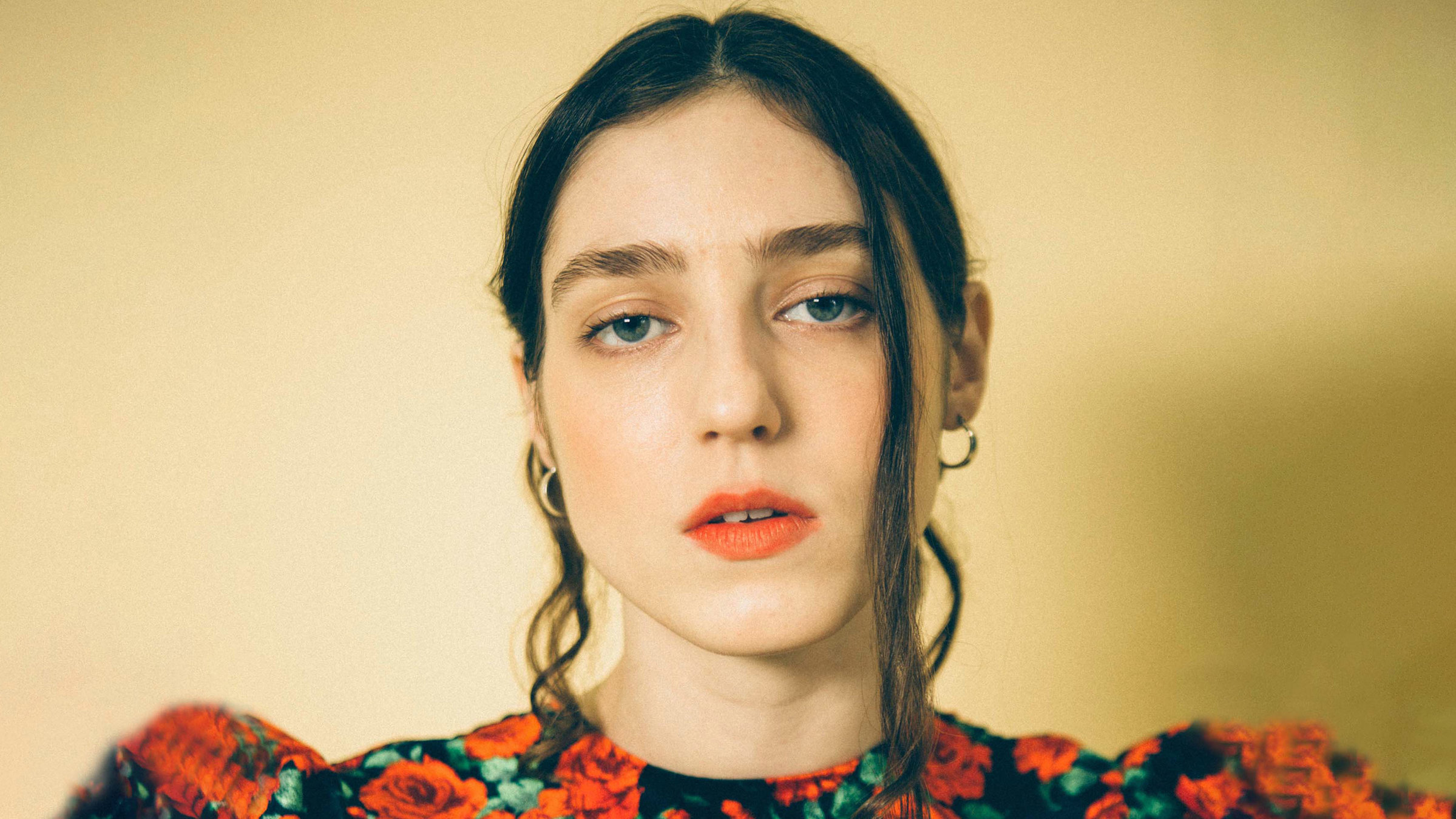 "Birdy: Live at Wiltons Music Hall": Eine Frau mit schwarzen zurückgebundenen Haaren schaut direkt ernst in die Kamera. Sie trägt goldene Ohrringe und ein schwarzes Oberteil mit roten Rosen.