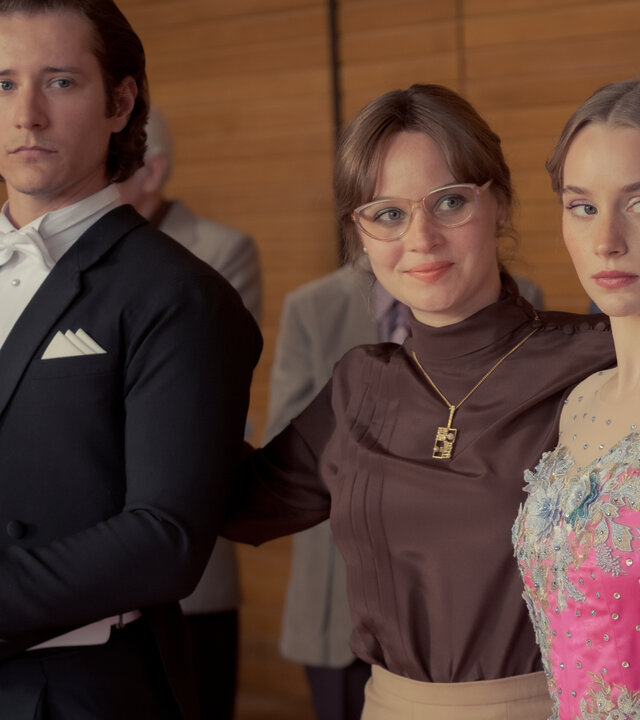 "Ku'damm 77": Steffen Henke (Benedikt Kalcher), Monika Franck-Schöllack (Sonja Gerhardt) und Dorli Schöllack (Carlotta Bähre) stehen nebeneinander in einer Sporthalle und blicken nach vorne.