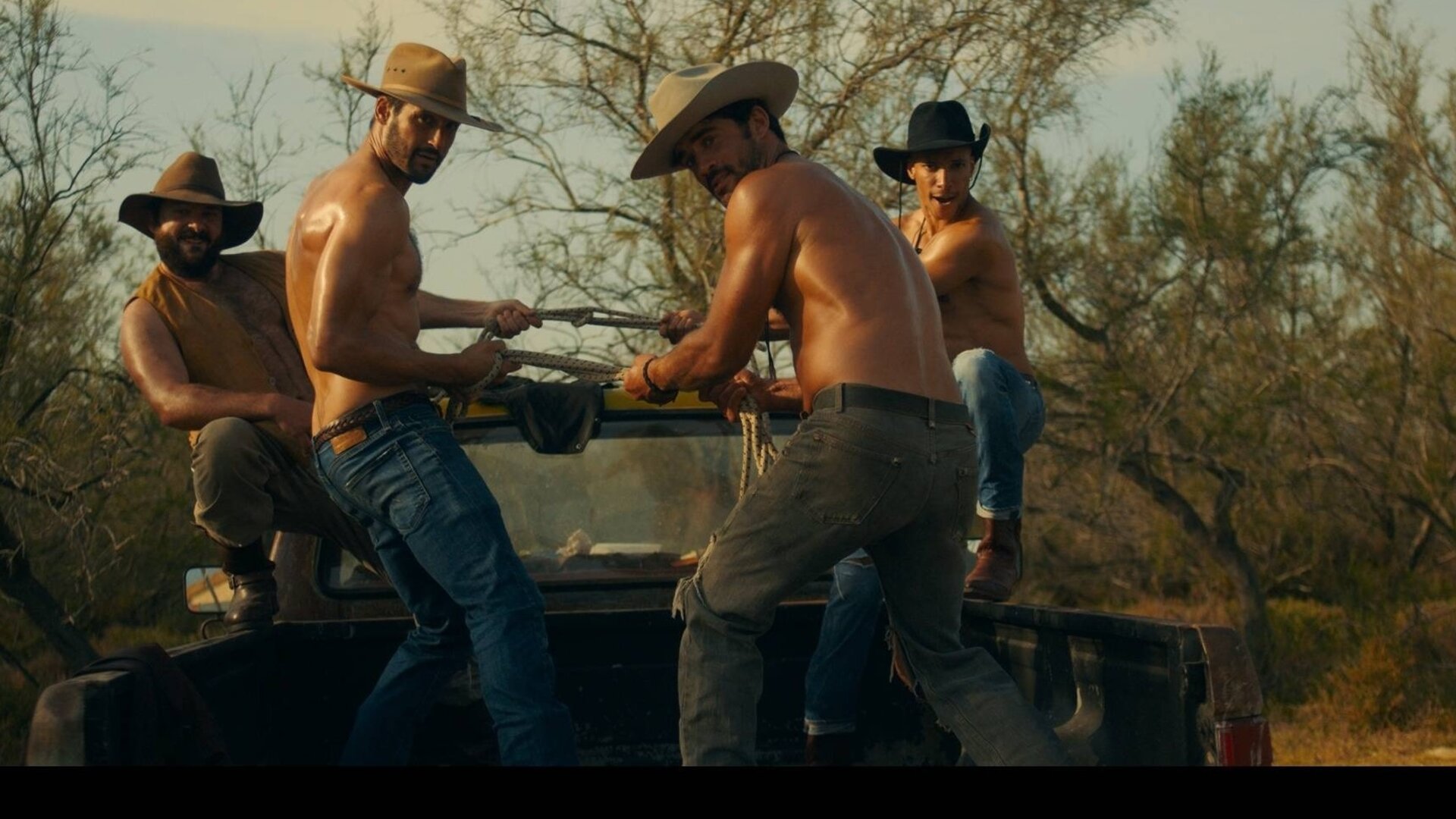 "Escort Boys - Honig ist die Zukunft": Ludo (Thibaut Evrard), Ben (Guillaume Labbé), Mathias (Simon Ehrlacher) und Zak (Corentin Fila) posieren auf der Ladefläche eines Pick-ups. Ludo und Zak hocken außen, Ben und Mathias stehen in der Mitte und halten gemeinsam ein Seil, an dem sie ziehen. Alle tragen Cowboyhüte - nur Ludo trägt zusätzlich eine offene gelbe Weste, die anderen sind oberkörperfrei.